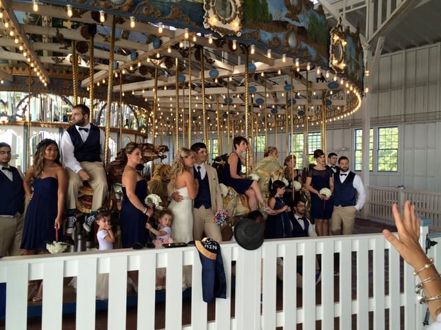 A wedding party gathered in front of a lit antique carousel