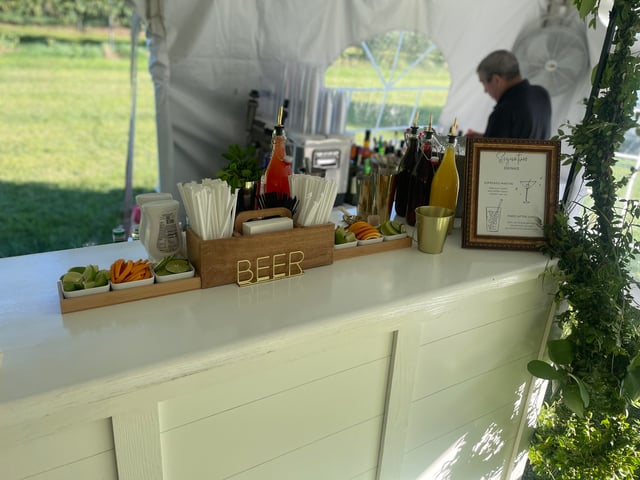 A paneled tent bar topped with fresh garnishes and a gold BEER sign
