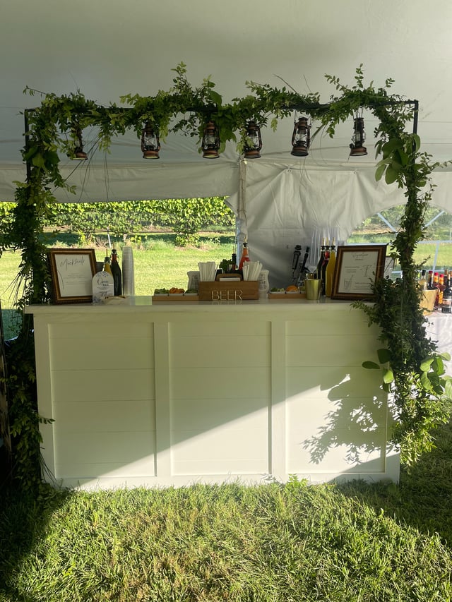 A white tent bar framed by a greenery arch hung with lanterns at a vineyard