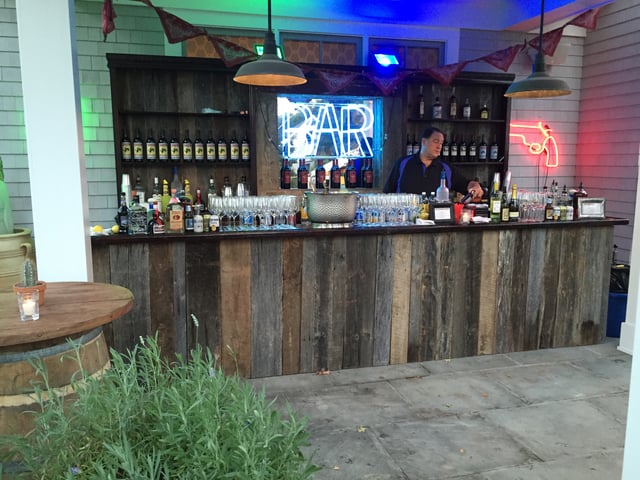 A reclaimed-wood event bar lit by a blue neon BAR sign