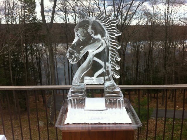 A carved horse ice sculpture on a deck overlooking the woods